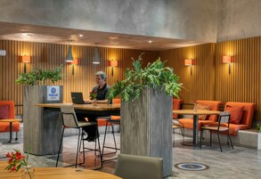 Un moderno vestíbulo de hotel con mostrador de recepción, zona de estar y plantas decorativas.