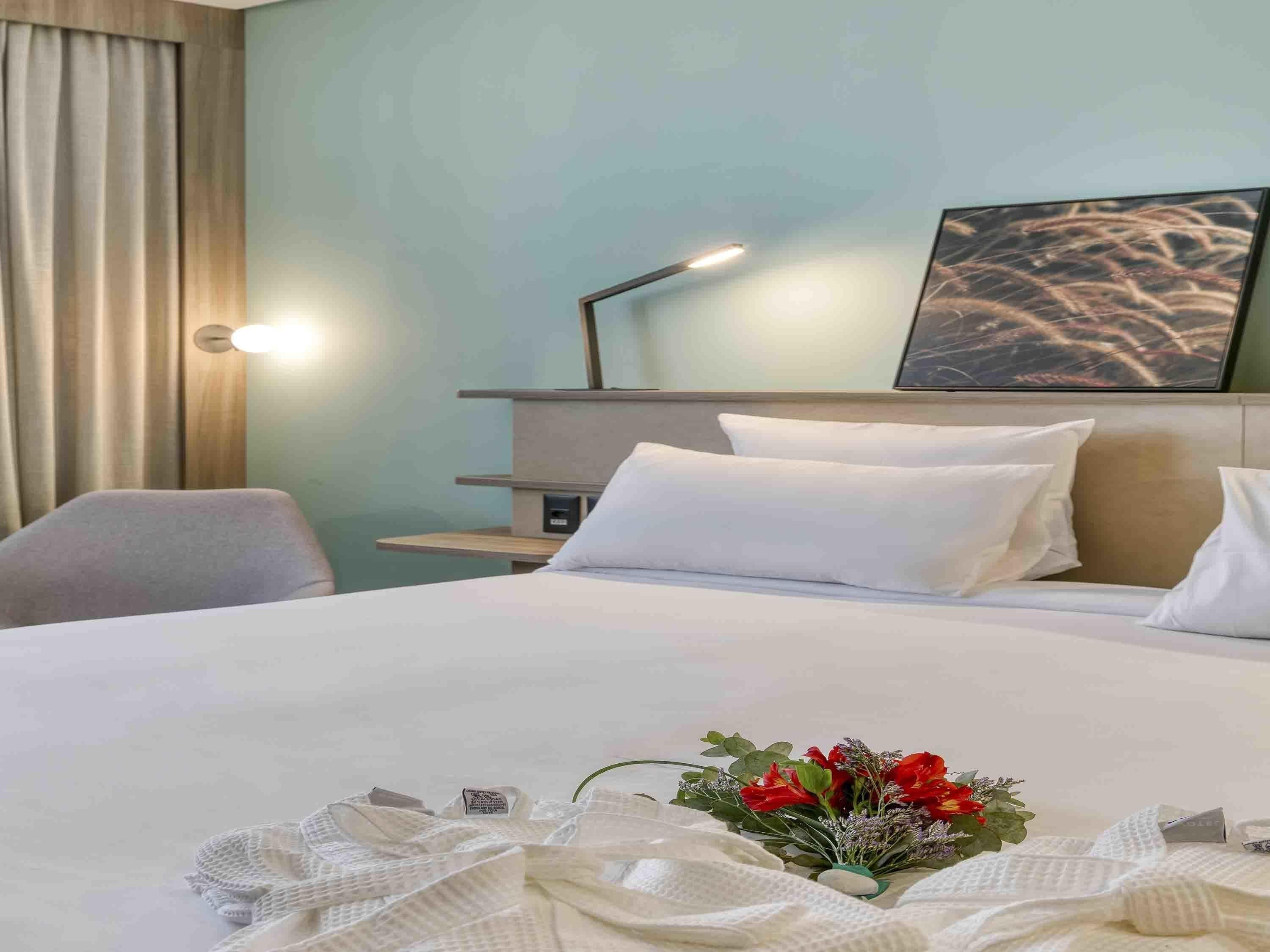 A hotel room with a bed, a desk, a chair, a lamp, and a painting on the wall.