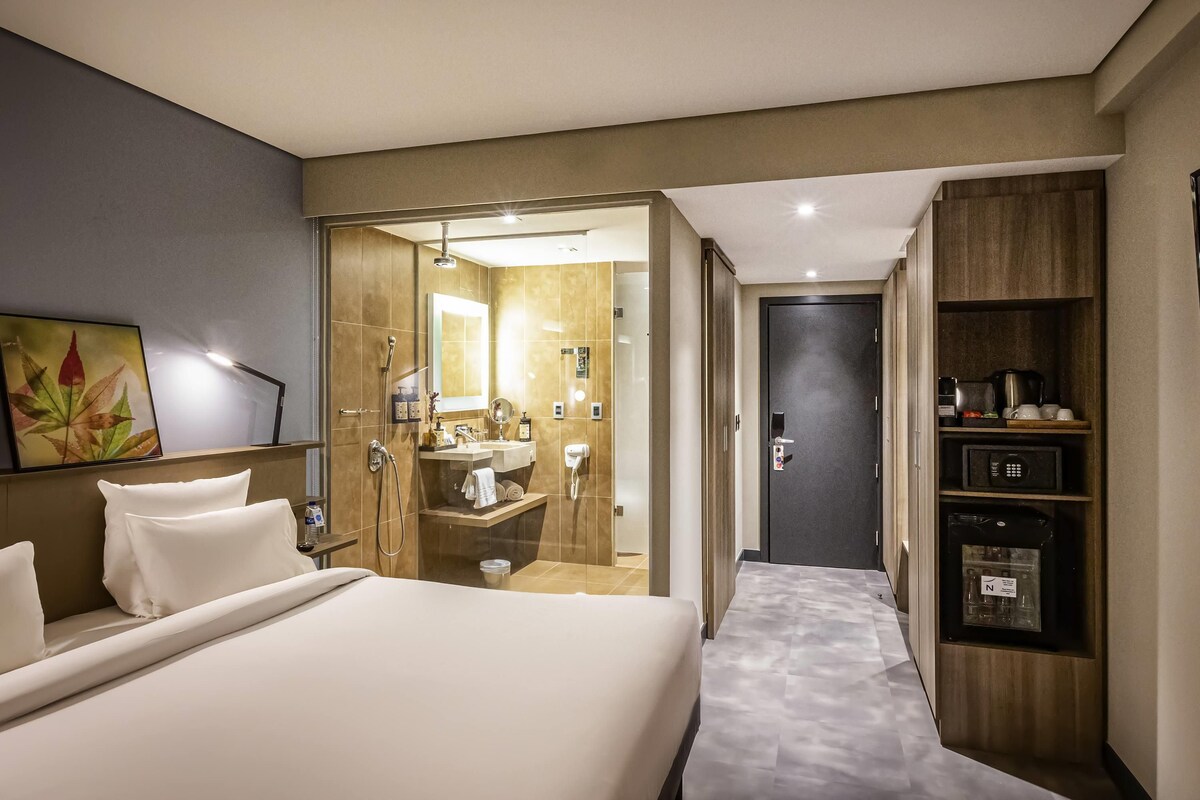 Habitación de hotel con cama, baño con ducha, lavamanos y armario.