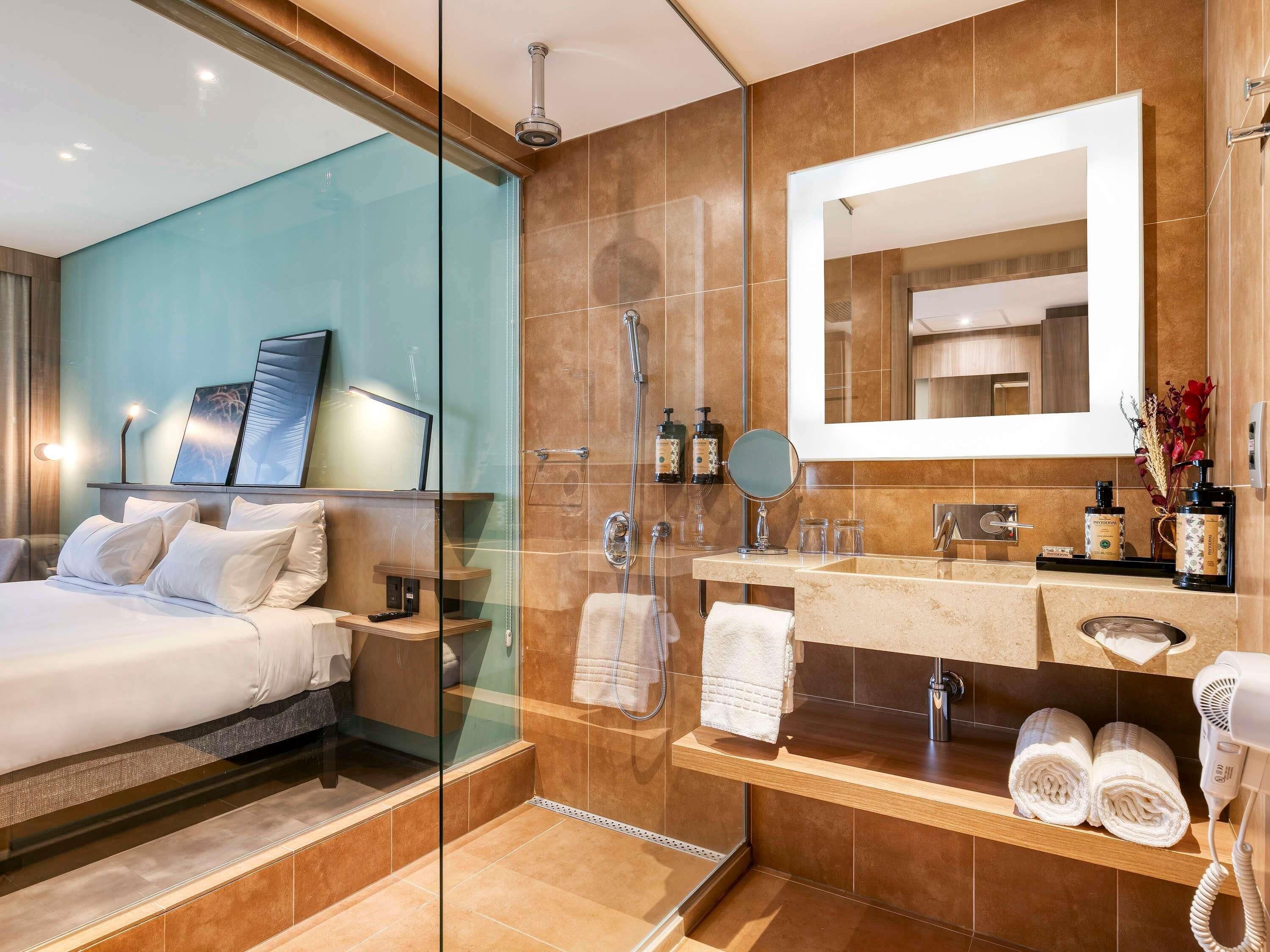 Une salle de bain d’hôtel moderne, dotée d’une douche à parois de verre, d’un grand miroir et d’un meuble-lavabo avec des articles de toilette.