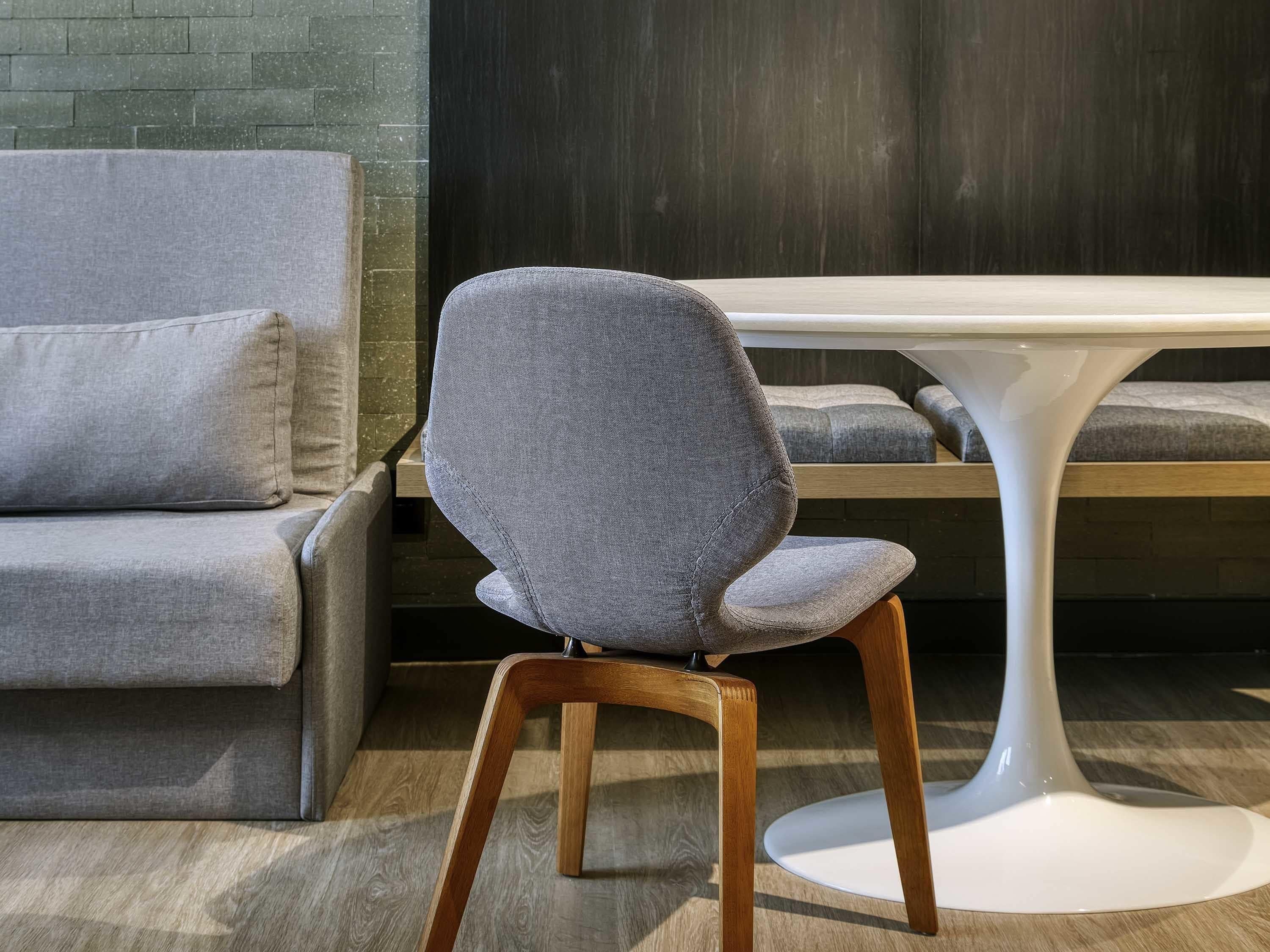 Una habitación moderna con un sofá tapizado en gris, una silla de madera y una mesa blanca.
