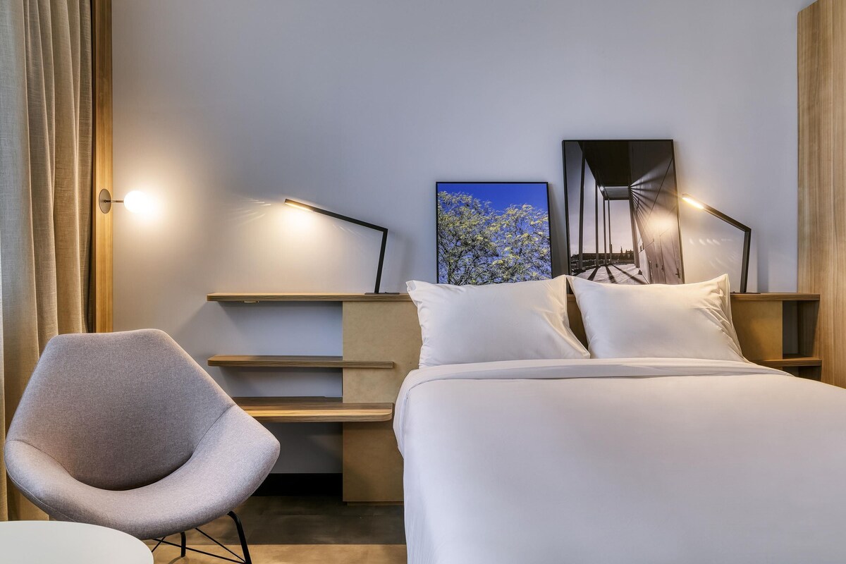 Une chambre d’hôtel avec un lit, une chaise, un bureau et un tableau au mur.
