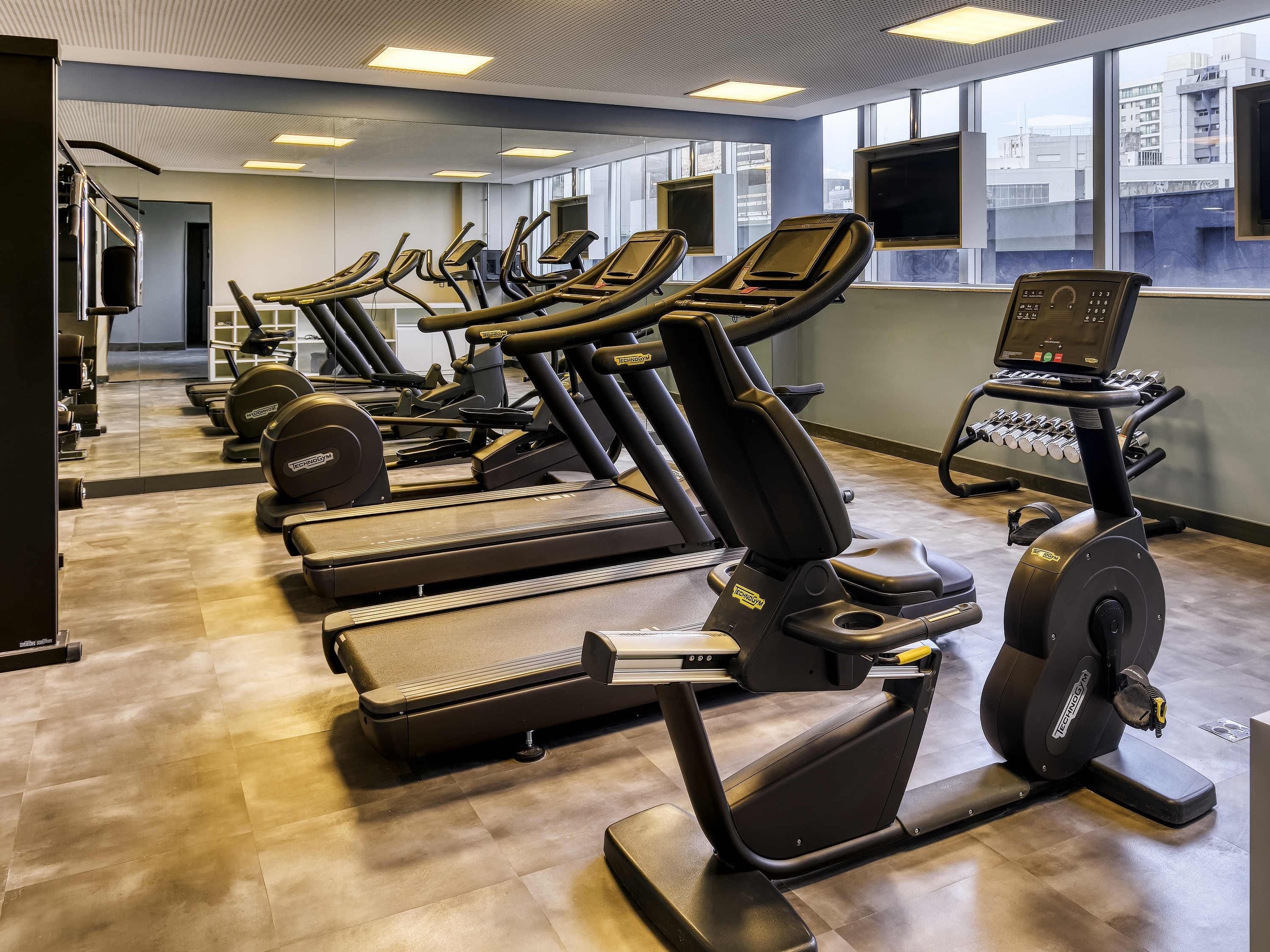 Een fitnessruimte met diverse loopbanden, krachttrainingsapparaten en een digitaal scherm.