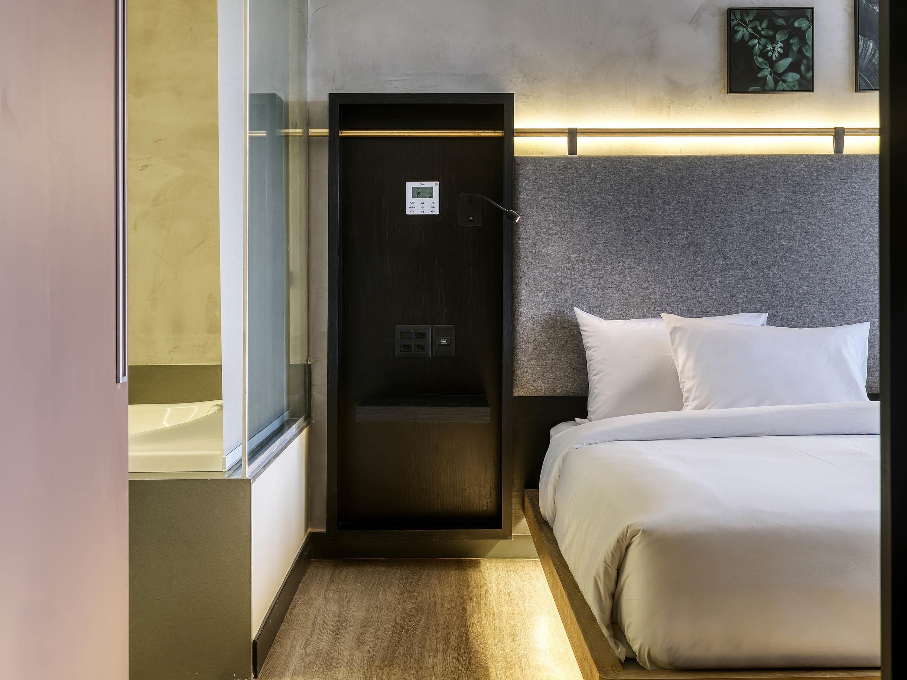 A hotel room with a bed, a control panel, and a door.