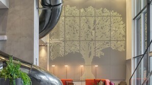Een moderne lobby met een gebogen metalen constructie, een zithoek met oranje banken en een decoratieve lichtwand.