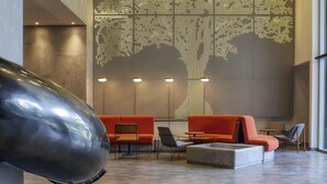 Een moderne lobby met een grote, verlichte muurschildering van een boom, een zithoek en een uniek metalen sculptuur.