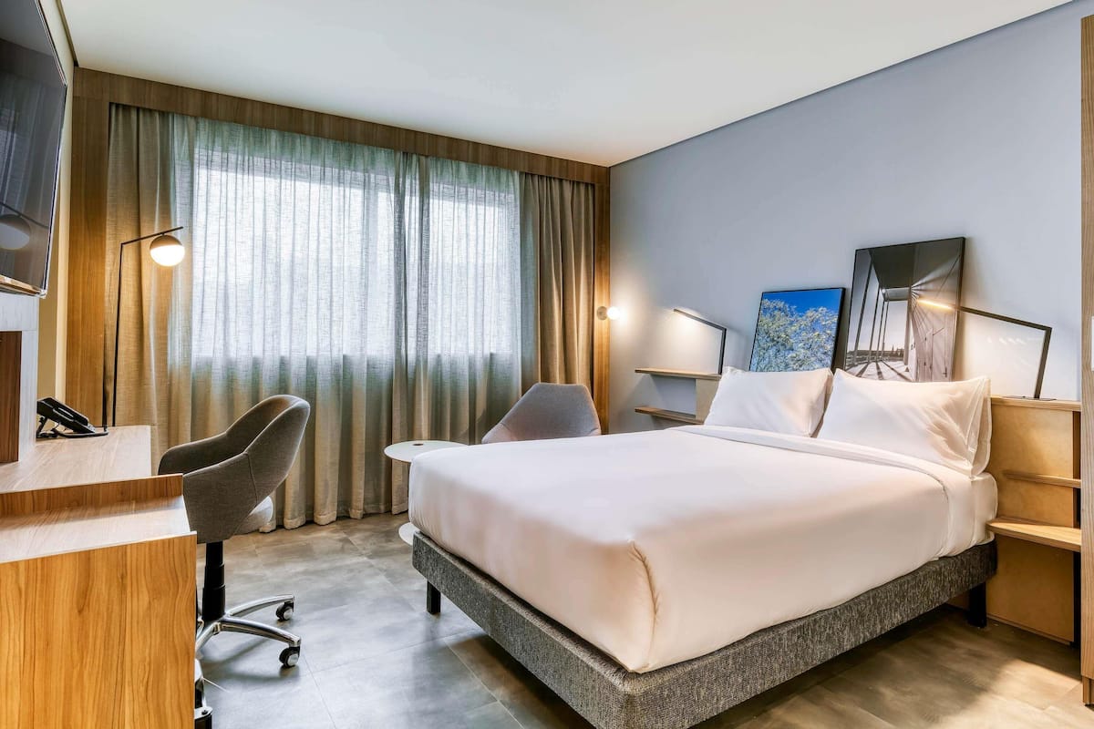 Habitación de hotel con cama, escritorio, sillas y un cuadro en la pared.