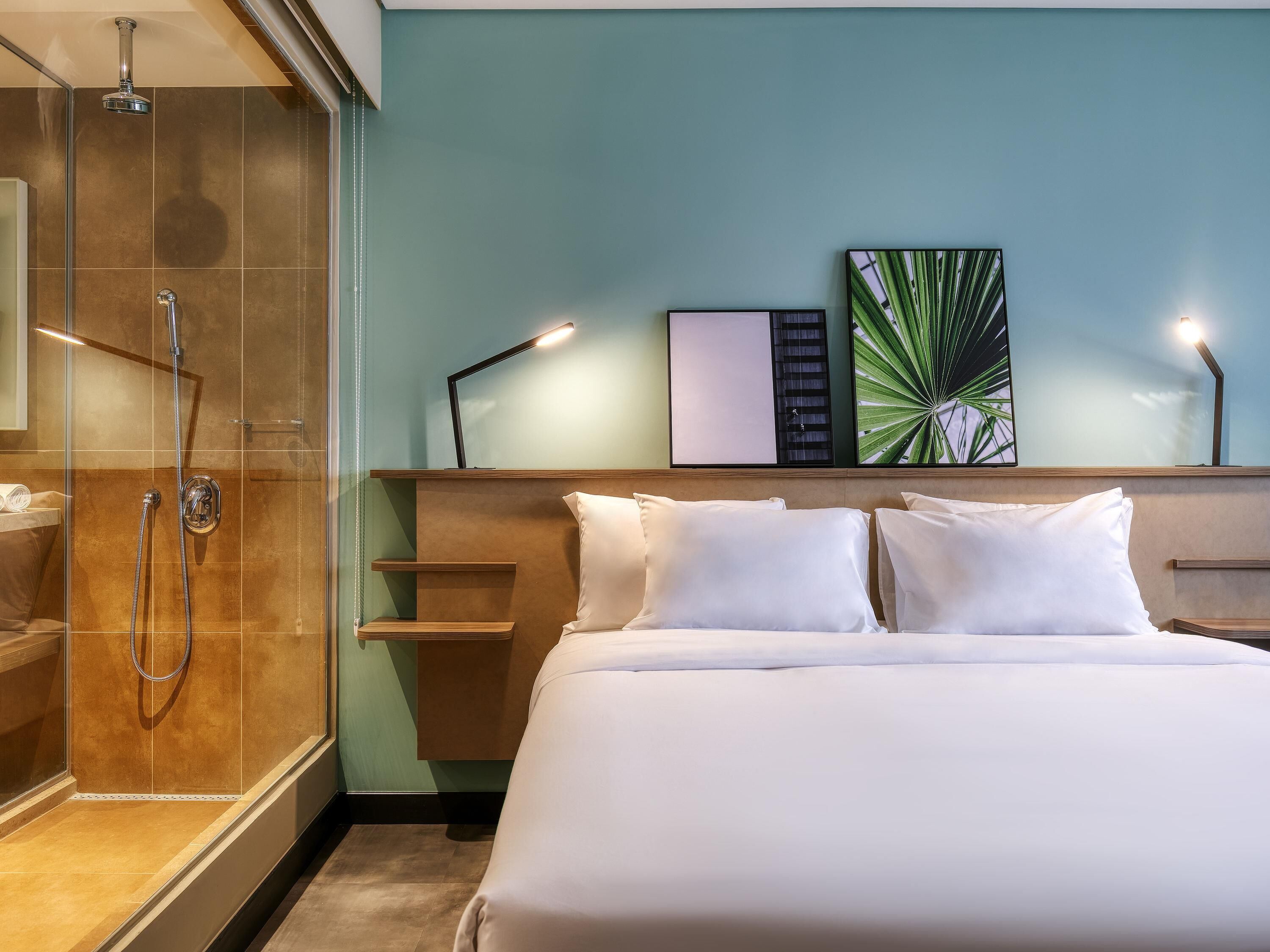 A hotel room with a shower, a bed with white linens, and a wall with artwork.