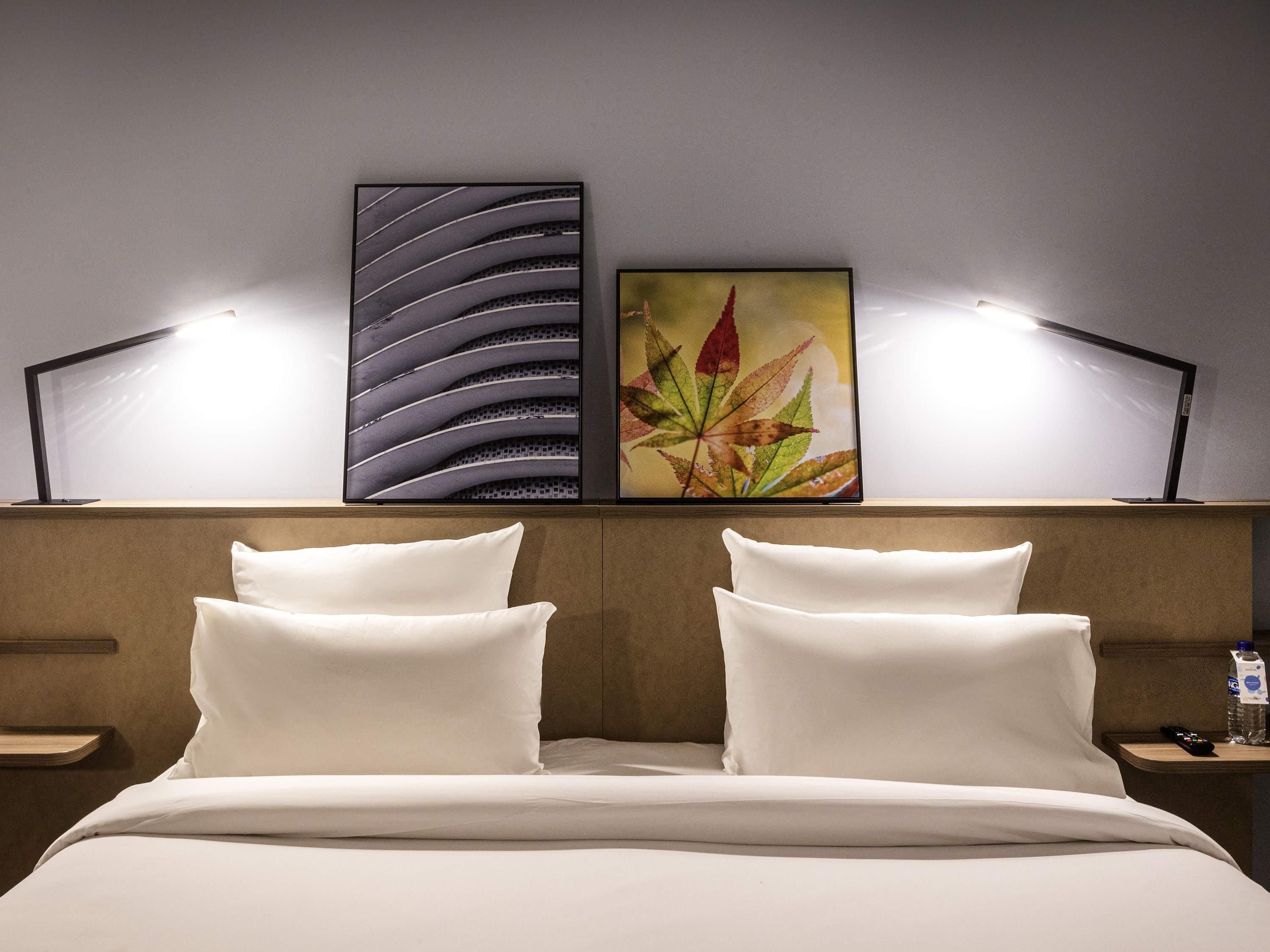 Een hotelkamer met een bed, twee bedlampen, een nachtkastje en twee kunstwerken aan de muur.