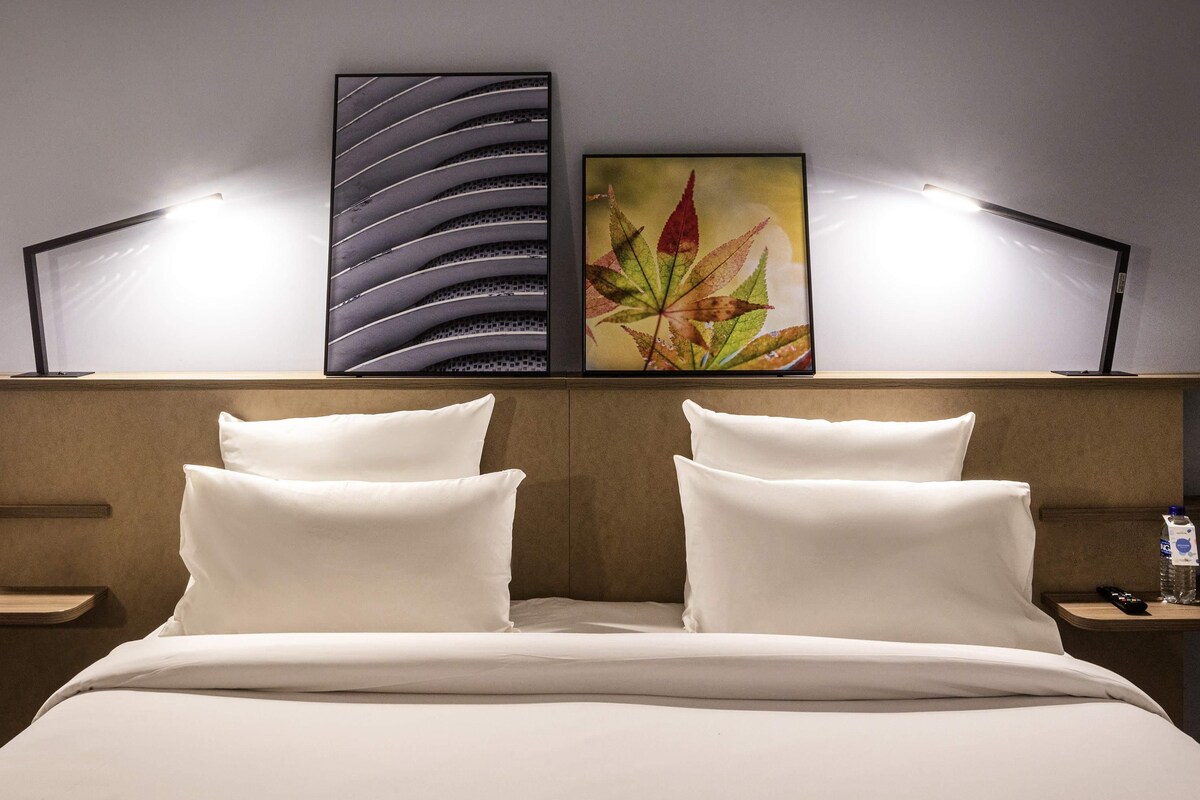 A hotel room with a bed, two bedside lamps, a nightstand, and two wall-mounted artworks.