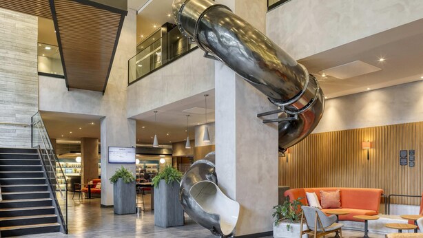 Een moderne lobby met een unieke spiraaltrap, zitgedeeltes en een digitaal informatiepaneel.