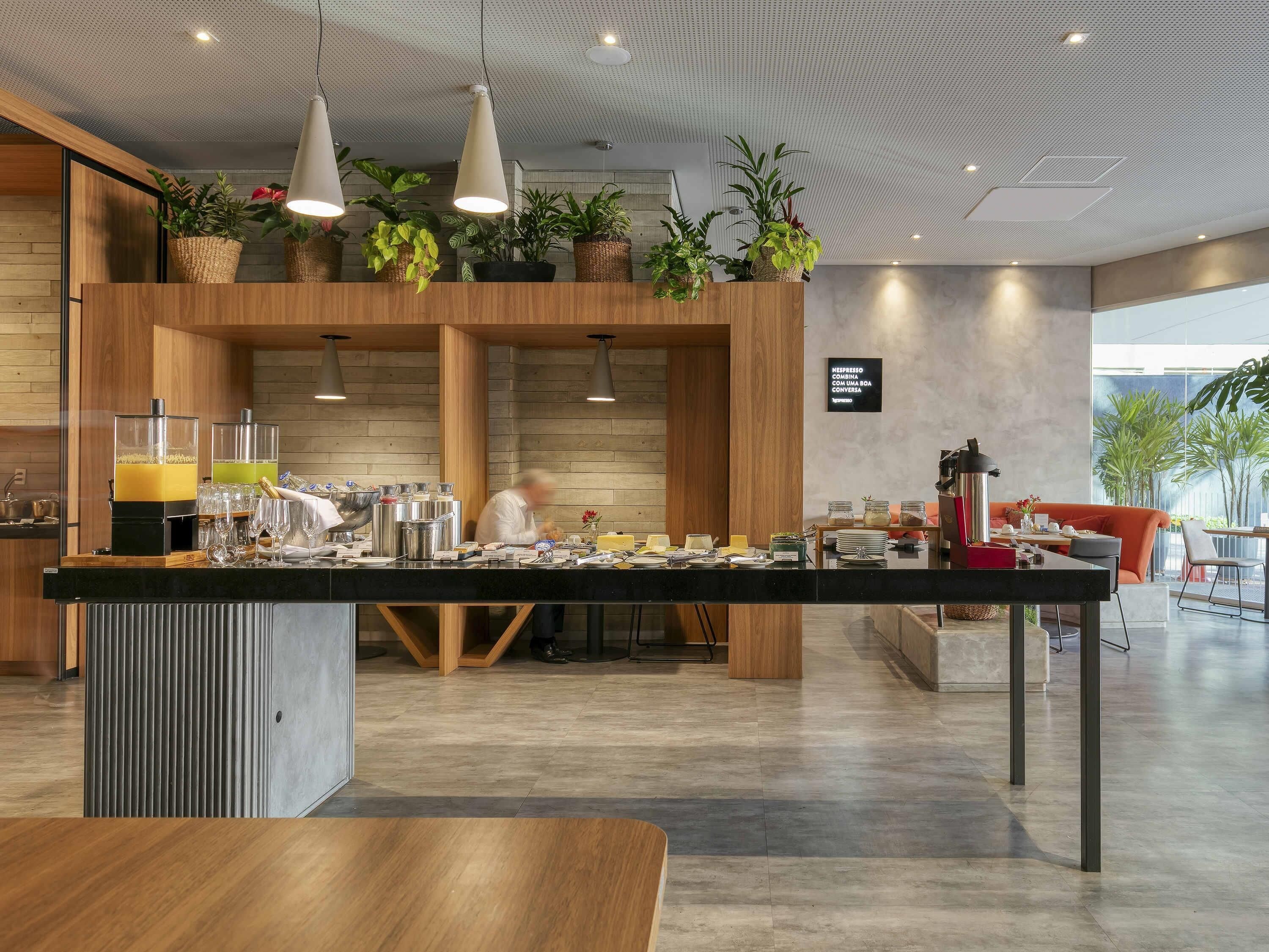 Un café moderno con mostrador de madera, plantas colgantes y una pizarra con el menú.