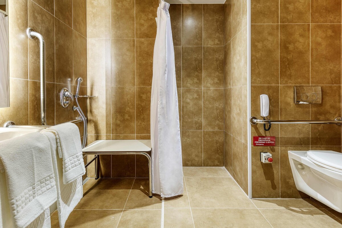 A bathroom with a shower, a toilet, and a handrail.