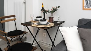 Um espaço compacto com uma mesa de jantar posta para dois, uma cadeira, um sofá e um radiador.