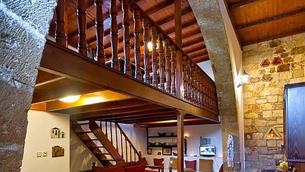 Ein geräumiger Loft mit hoher Decke, freiliegenden Holzbalken, einer Steinwand und einem Essbereich mit Tisch und Stühlen.