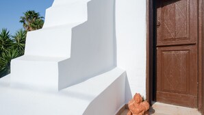 Eine weiße Treppe führt zu einer braunen Tür, am Fuß befindet sich eine kleine Terrakotta-Statue.