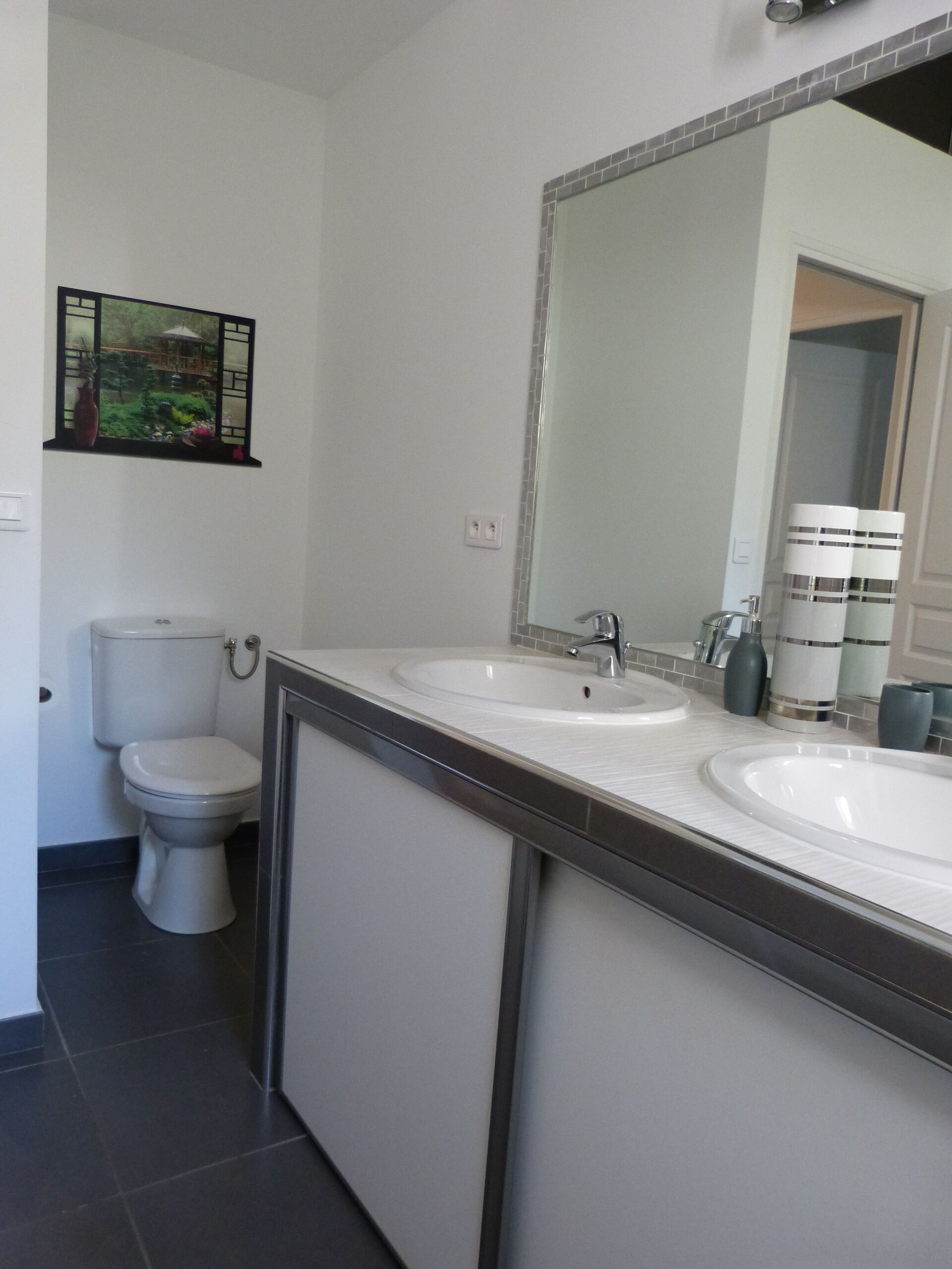 Un baño moderno con dos lavamanos, un inodoro y un espejo grande.