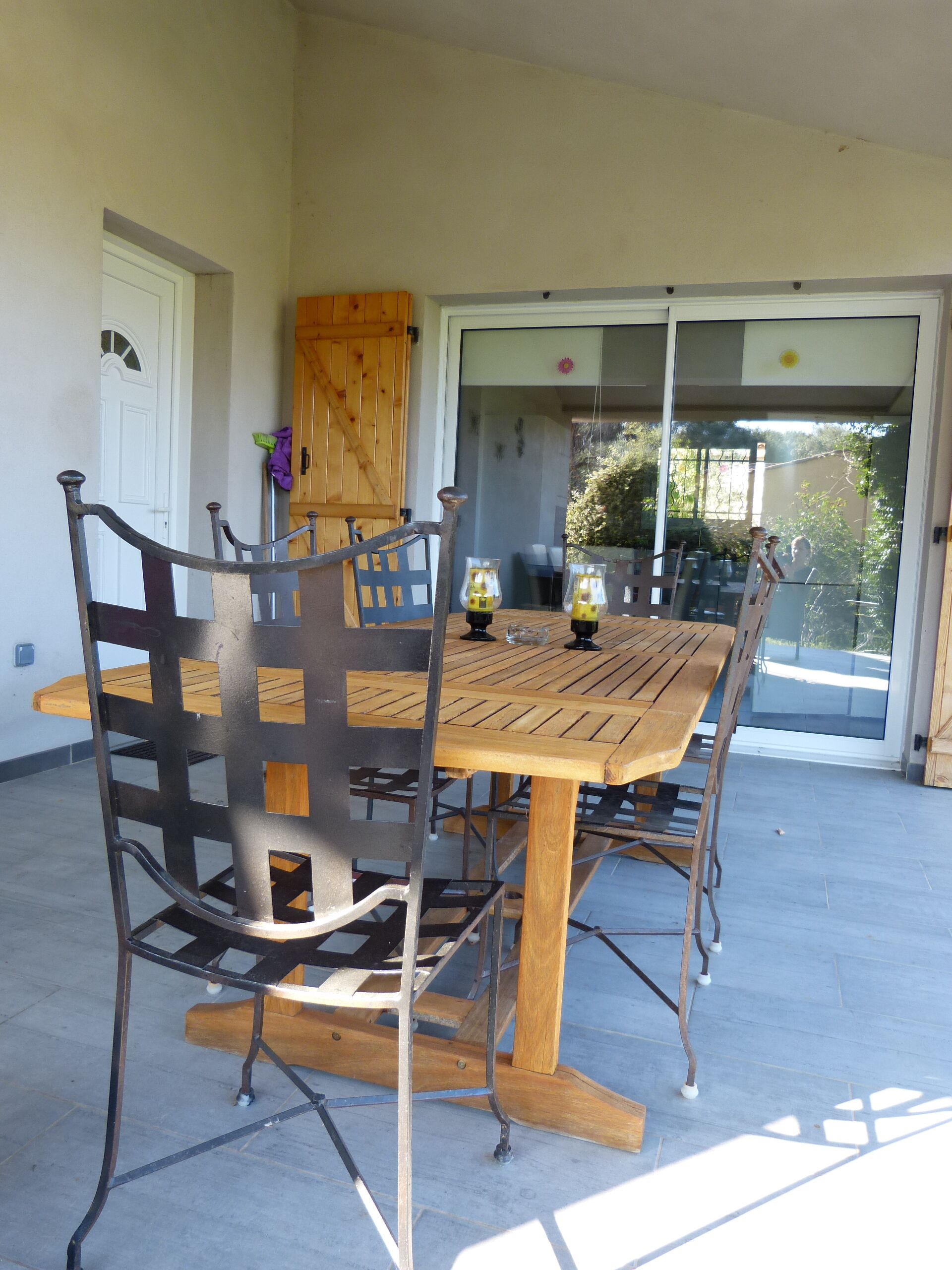 Une terrasse avec une table en bois et des chaises en métal, une porte-fenêtre coulissante et un meuble en bois.