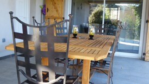 Une terrasse avec une table en bois et des chaises en métal, une porte-fenêtre coulissante et un meuble en bois.