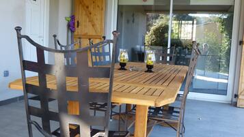 Une terrasse avec une table en bois et des chaises en métal, une porte-fenêtre coulissante et un meuble en bois.