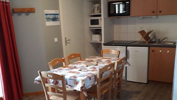 Kompakti oleskelutila, jossa on ruokapöytä, tuolit, sohva, keittiöalue kodinkoneineen ja puulattia.