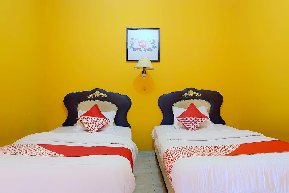 Une chambre avec deux lits, chacun doté d’une tête de lit, d’une lampe fixée au mur et d’un tableau encadré au-dessus des lits.