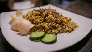 A plate of fried rice with vegetables and two dumplings, accompanied by cucumber slices.