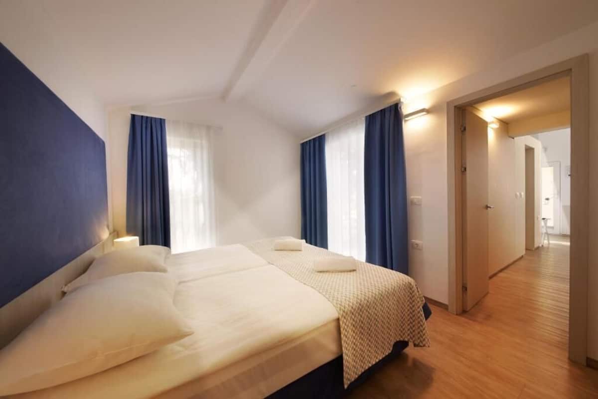 A hotel room with two beds, a wooden floor, and a hallway leading to another room.