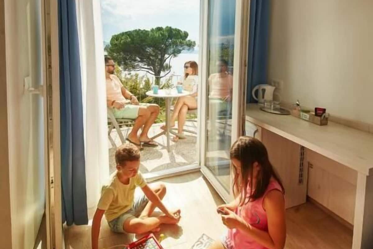 A room with a sliding glass door leading to an outdoor seating area. Inside, there is a child playing with toys on the floor, and a woman sitting on the floor.