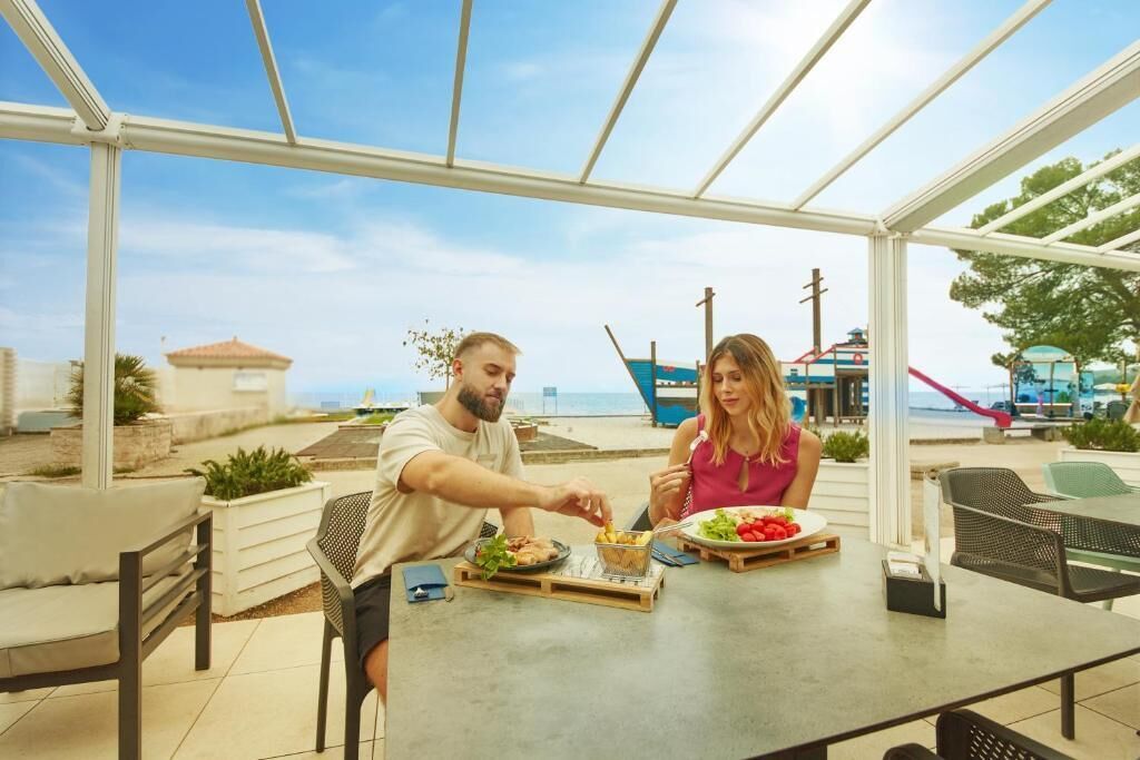 Una coppia cena a un tavolo all'aperto con vista sul mare e una barca sullo sfondo.