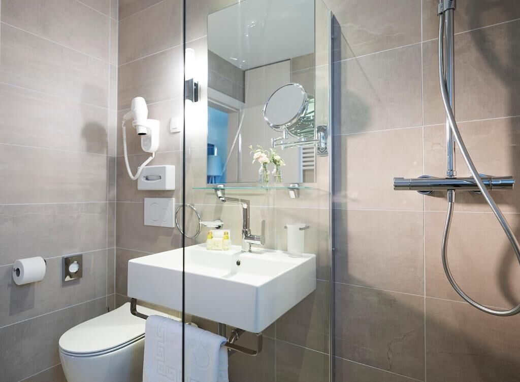 Un baño moderno con cabina de ducha de vidrio, un lavamanos blanco, un inodoro y un espejo.