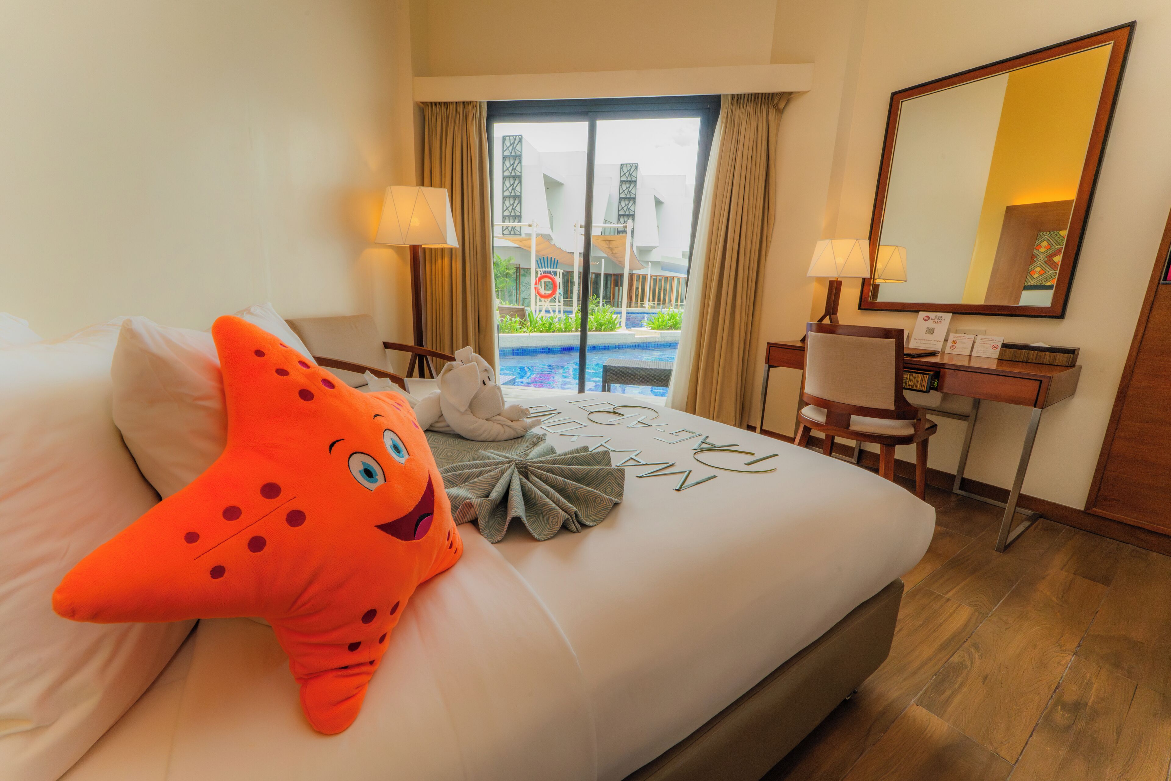 A hotel room with a bed, a desk, a chair, a large mirror, and a view of a swimming pool.