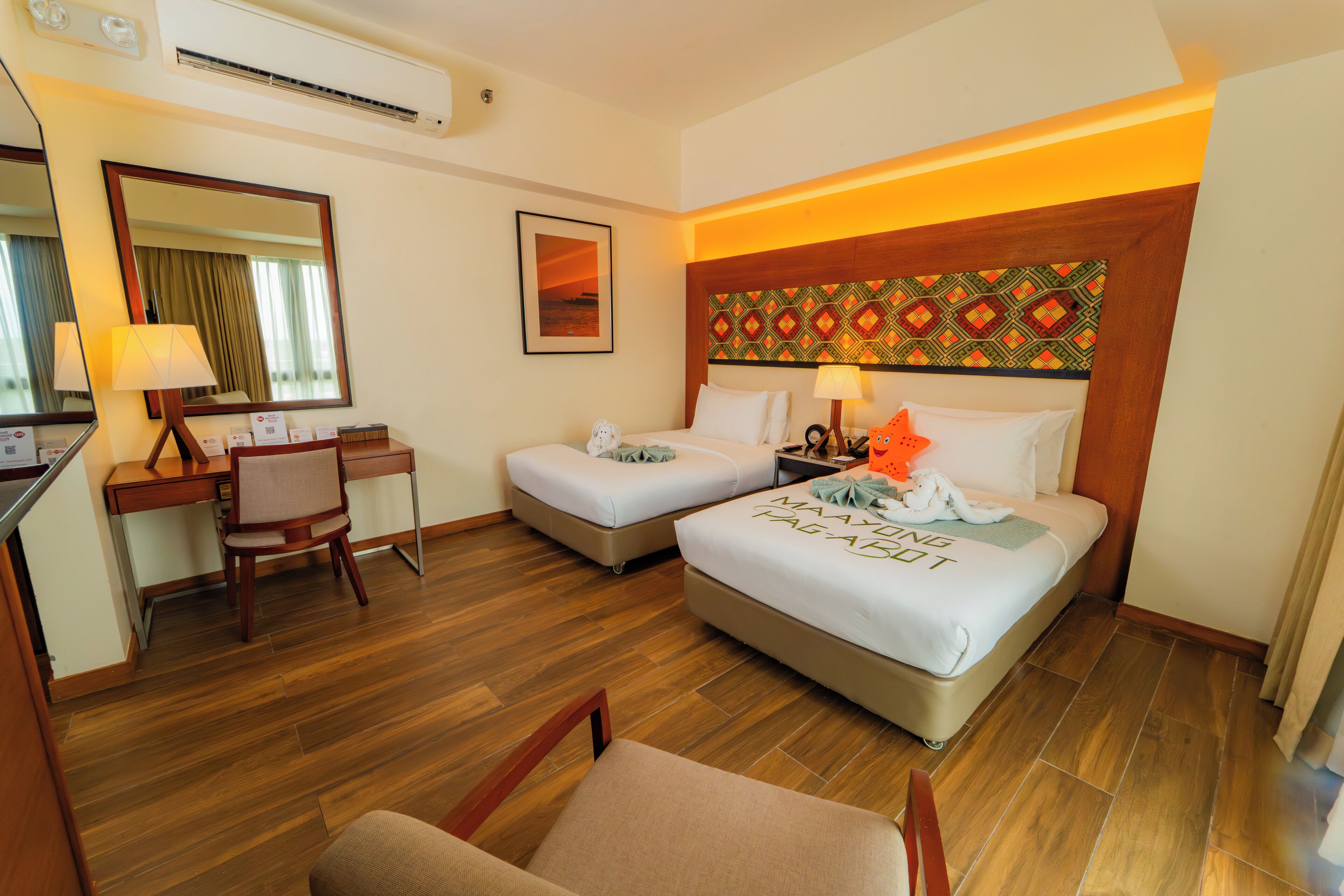 A hotel room with two beds, a desk, a chair, and a large mirror.