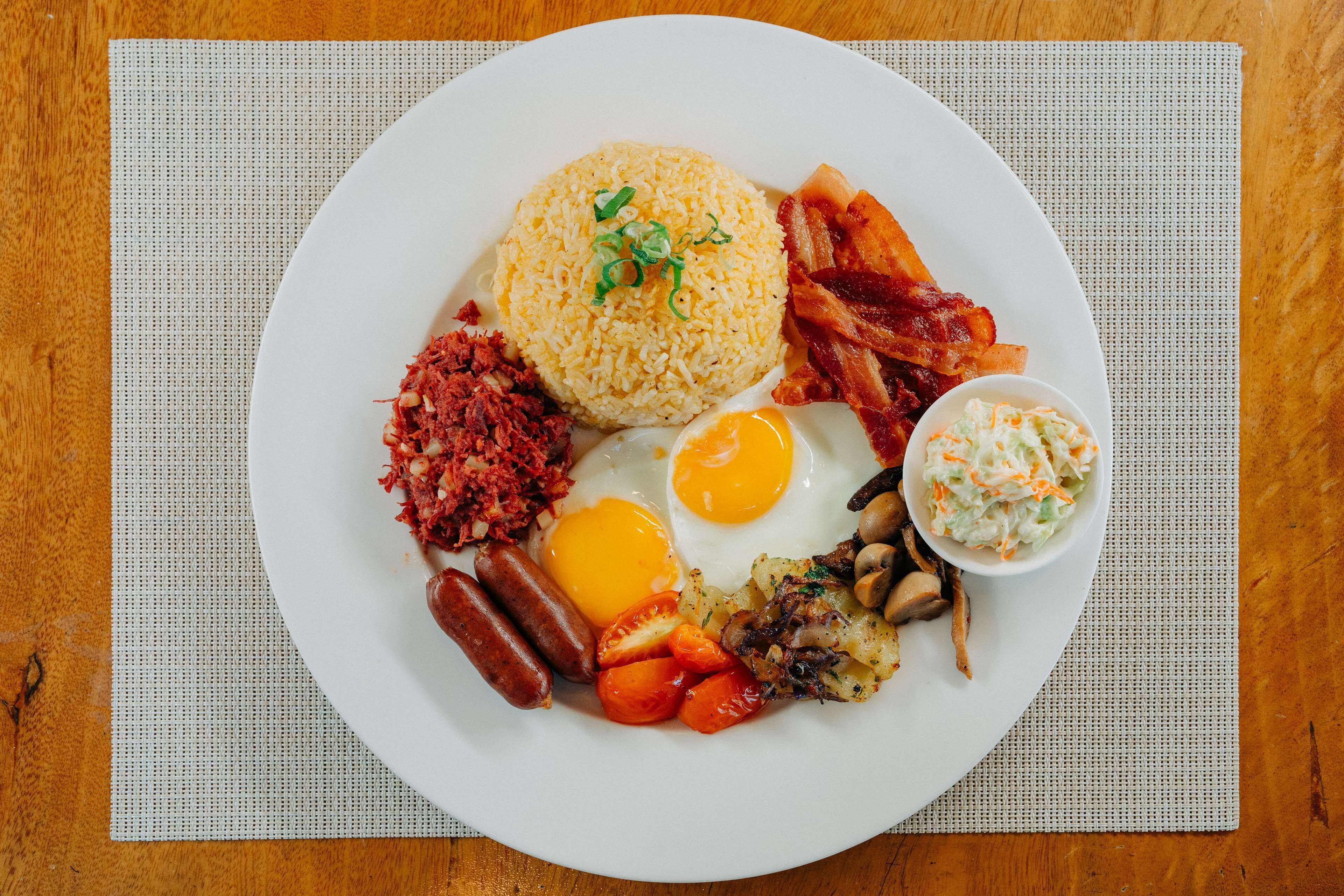 A plate of breakfast food including eggs, sausages, bacon, and rice.