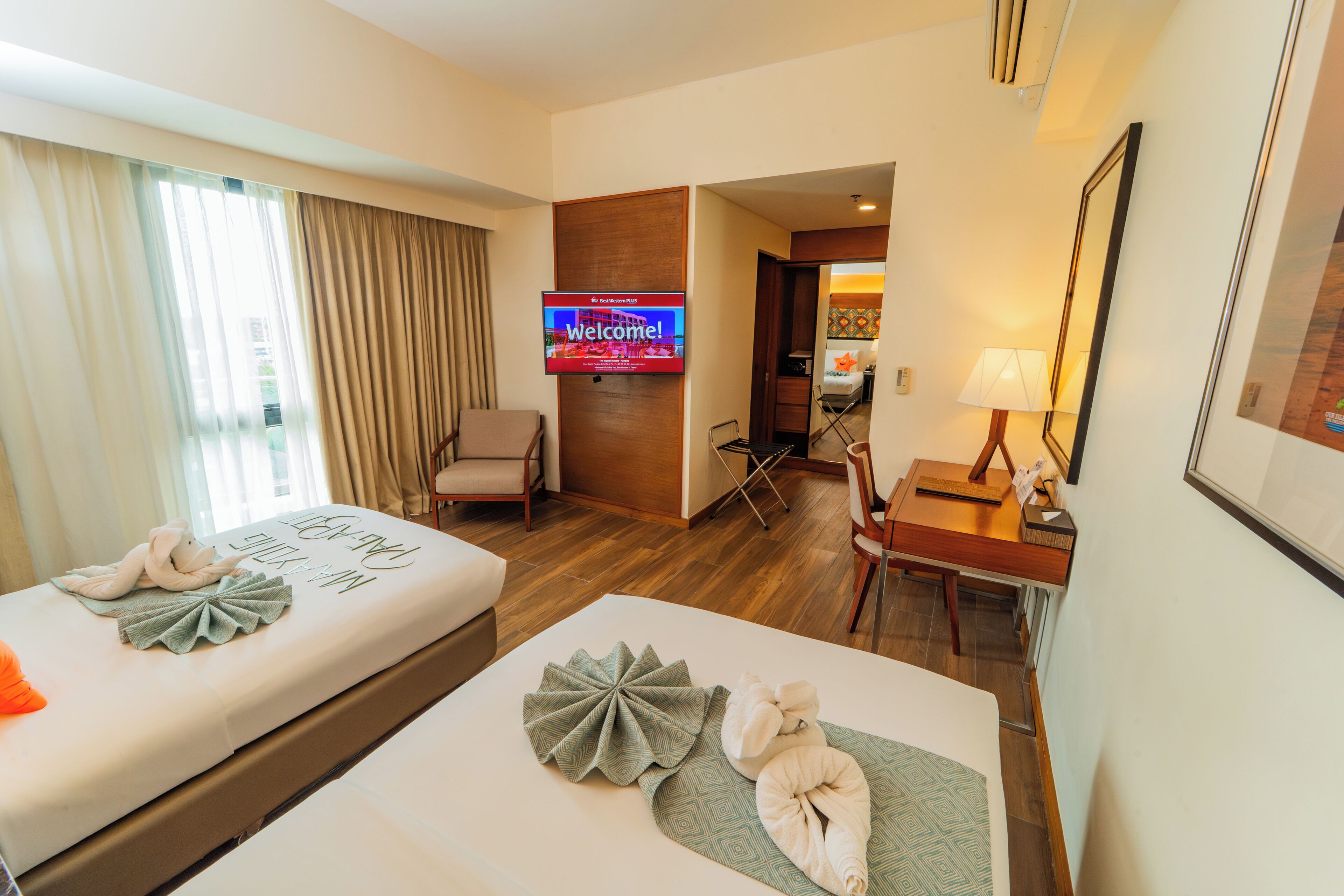 Ein Hotelzimmer mit zwei Betten, einem Fernseher, einem Schreibtisch und einem Stuhl.