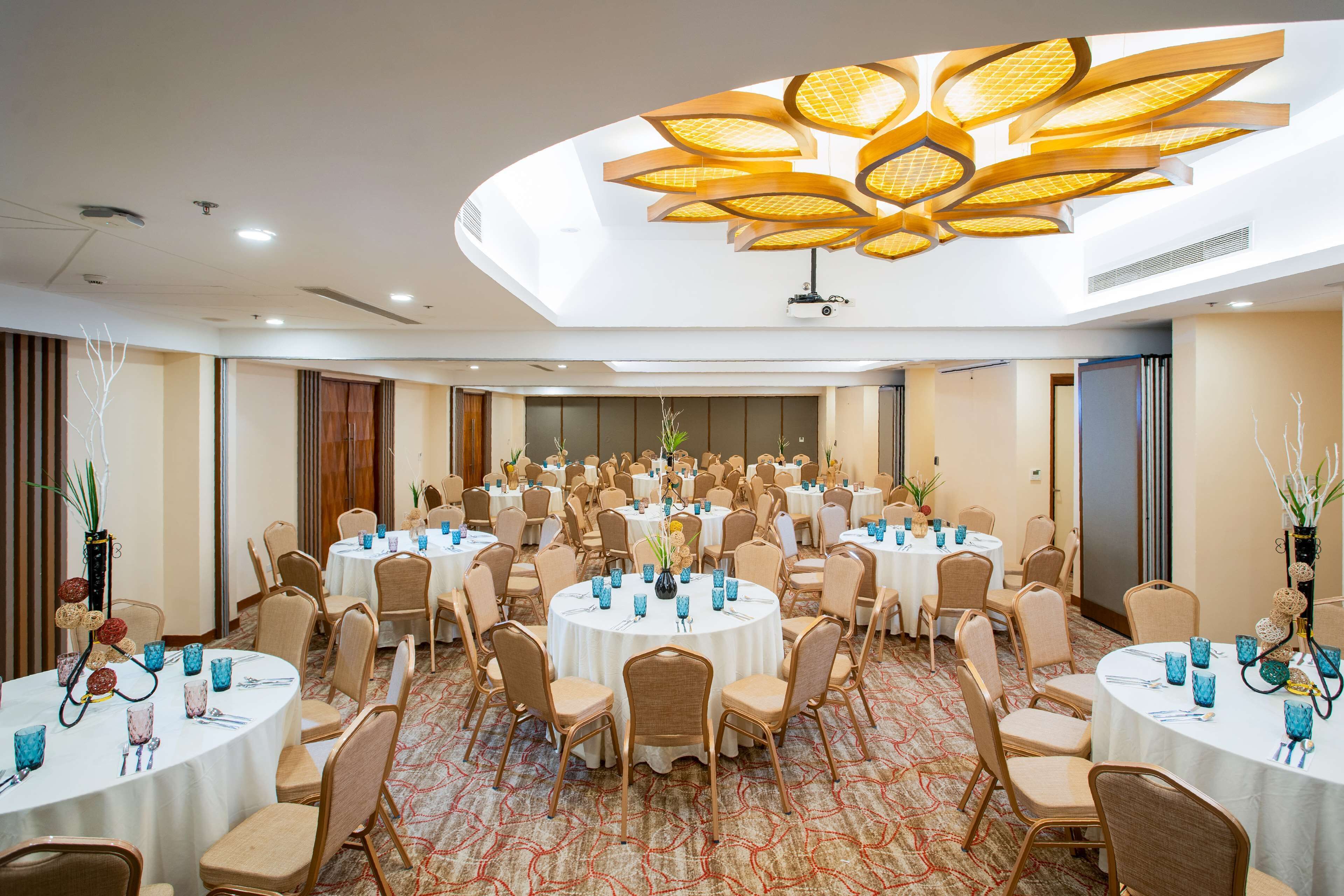 Une salle de conférence dotée de plusieurs tables rondes, chacune étant agrémentée de chaises et de verres bleus.