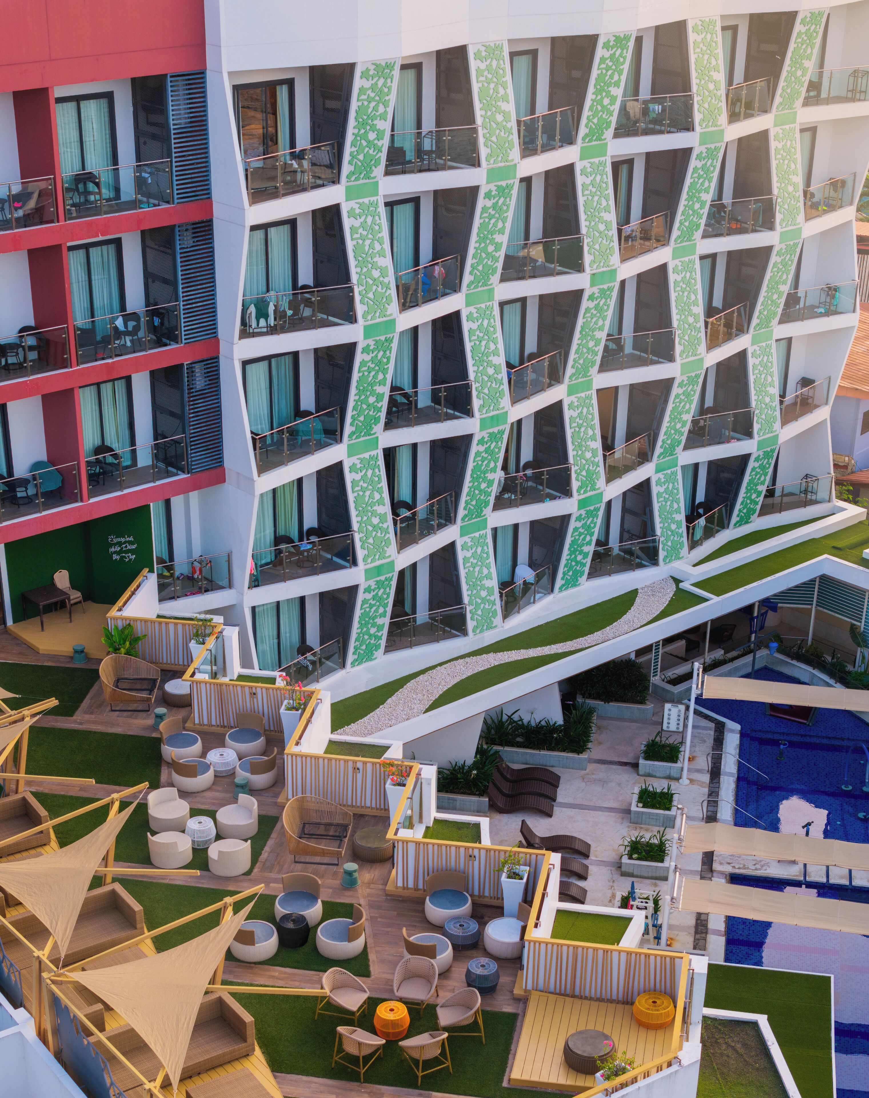 A modern hotel with multiple balconies, outdoor seating areas, and a pool.