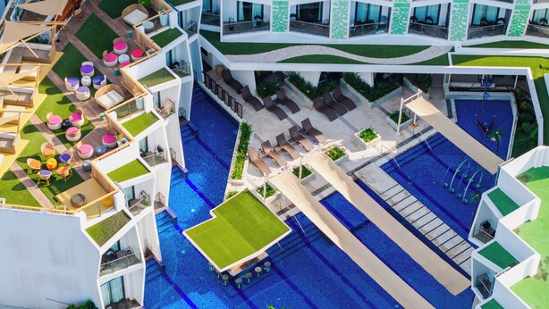 A multi-level hotel with a rooftop pool, outdoor seating areas, and a central swimming pool.
