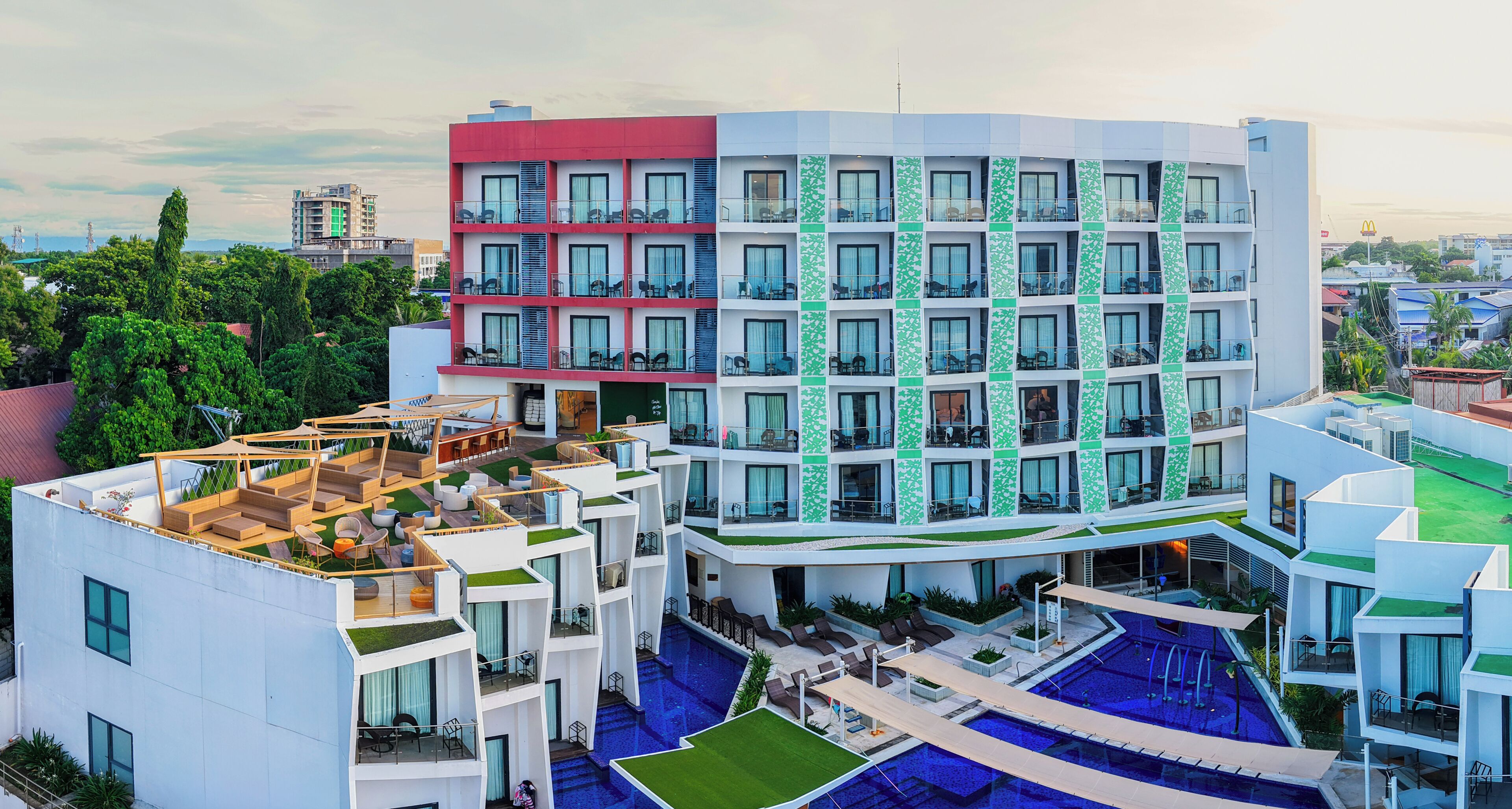 A multi-story hotel with a rooftop pool area, multiple balconies, and a modern architectural design.