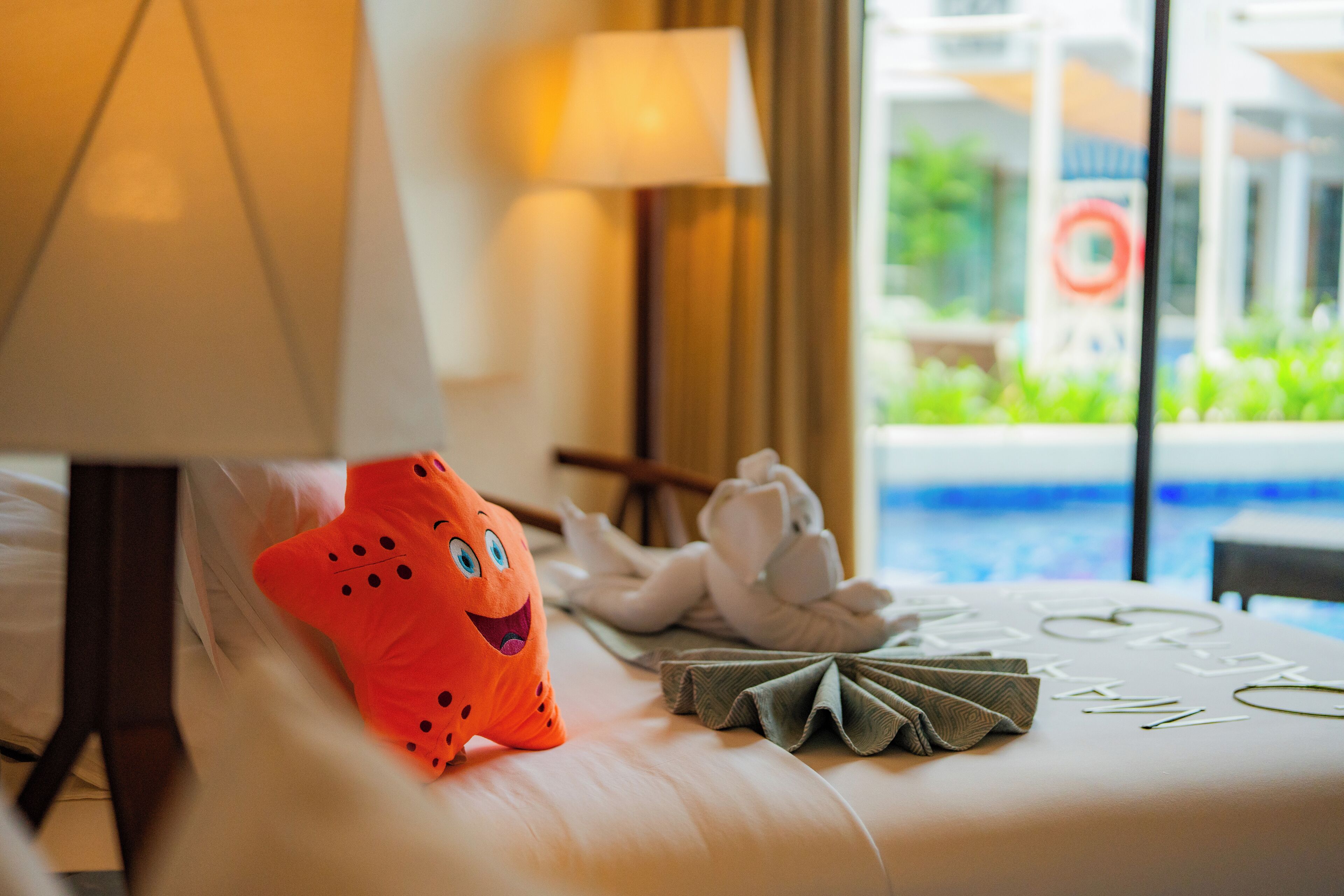 A hotel room with a bed, a lamp, a plush toy, and a view of a pool.
