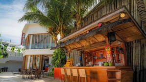 A bar area with wooden furniture and a tropical theme, including palm trees and a bamboo structure.