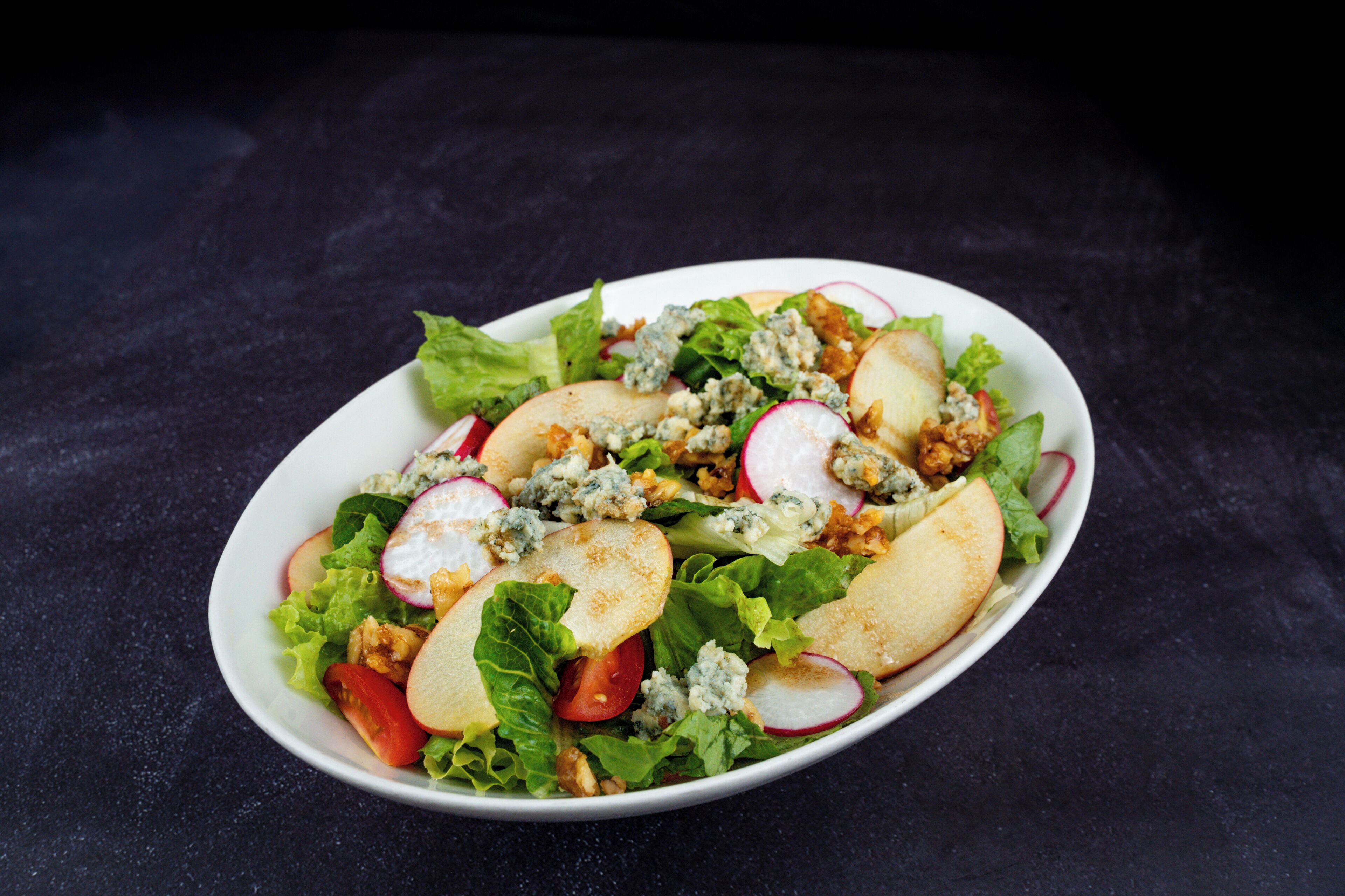 A salad with lettuce, radishes, tomatoes, and blue cheese on a white plate.