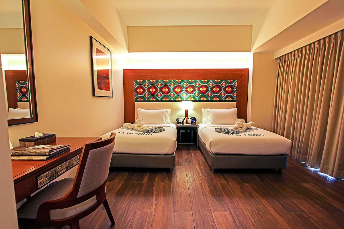 A hotel room with two beds, a desk, a chair, a mirror, and a patterned headboard.