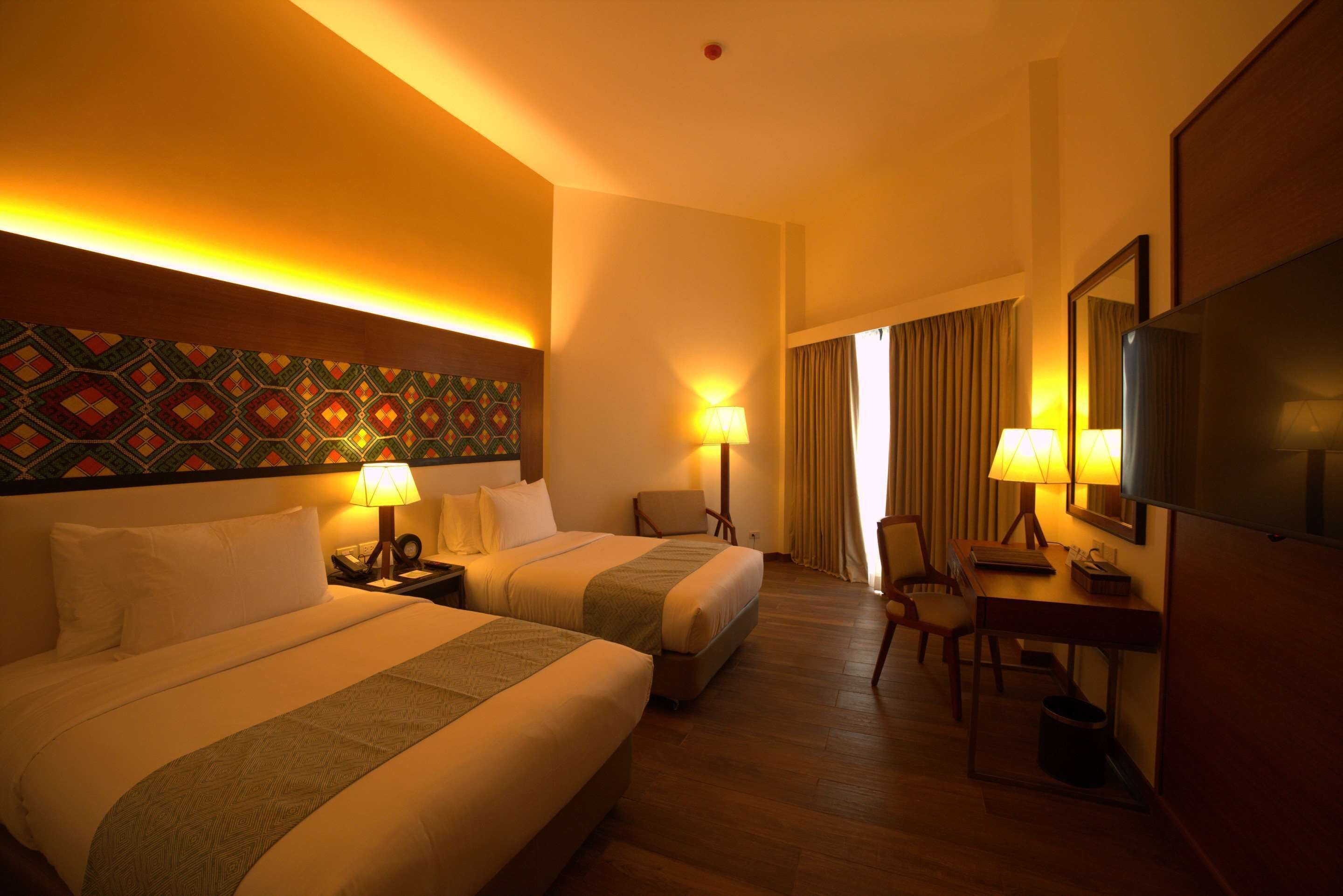 Een hotelkamer met twee bedden, een bureau, een stoel, een televisie en een bed met een patroon.