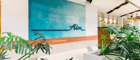 Un área de recepción con una gran pared azul, un mostrador de madera y plantas tropicales.