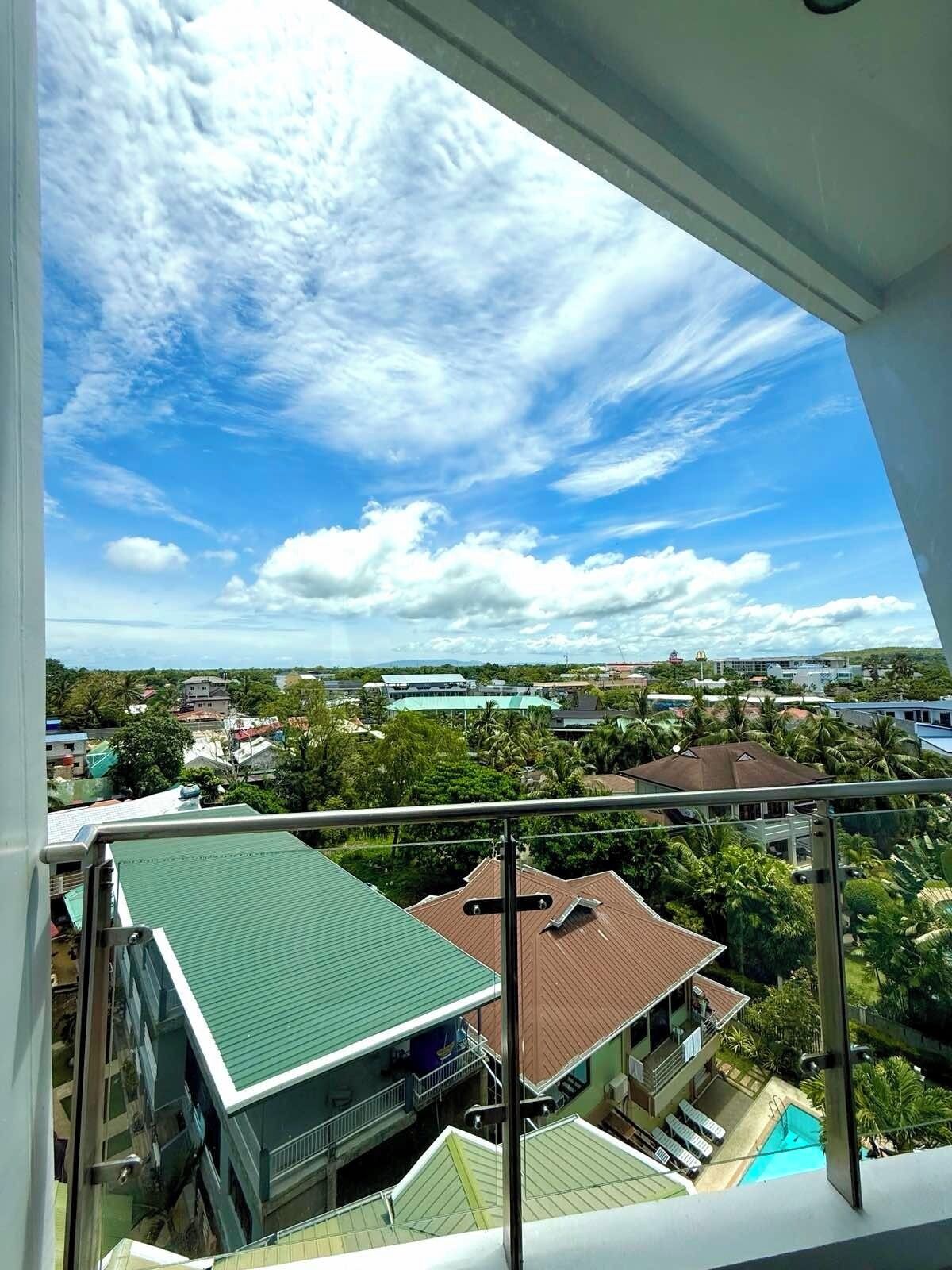 A view from a balcony with a clear sky, a swimming pool, and surrounding buildings.