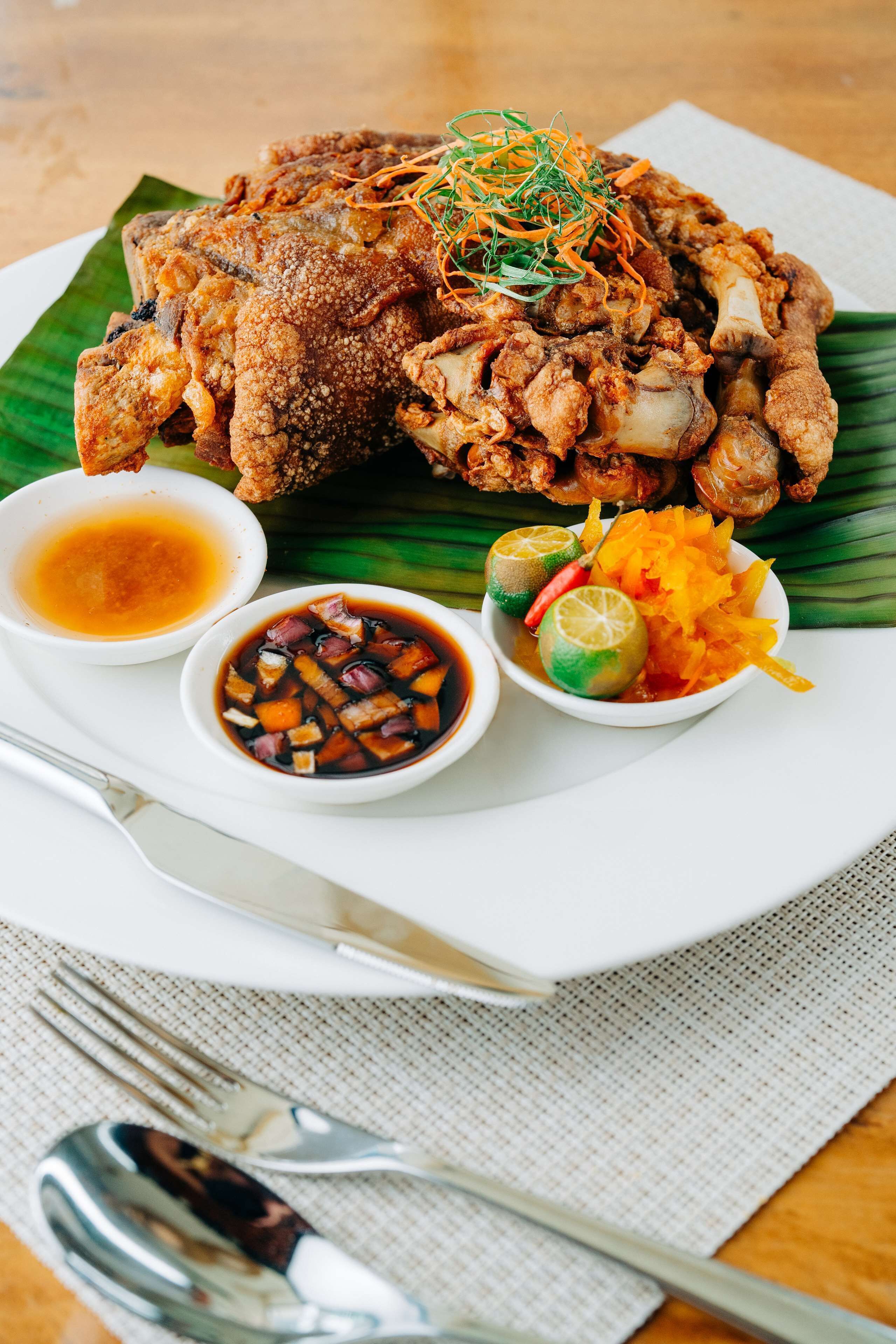 Un plato de pollo frito acompañado de salsa para mojar y verduras encurtidas.
