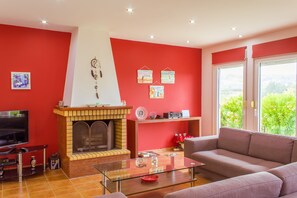 A living room with a fireplace, a sofa, a TV, and a large window with a view.