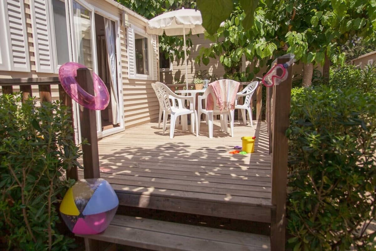 Een houten terras met een tafel en stoelen, omringd door groen.