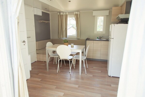 Een compacte keuken met een eethoek, houten vloeren en een raam met gordijnen.